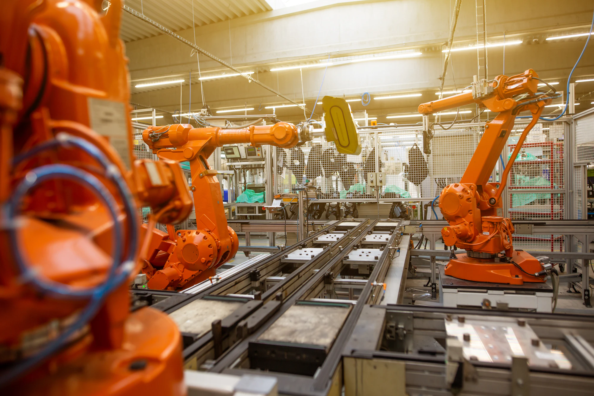 Orange industrial robot arms beside production equipment.