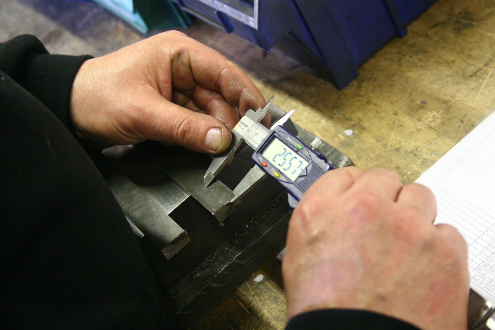 Hands using digital calipers on a metal component.